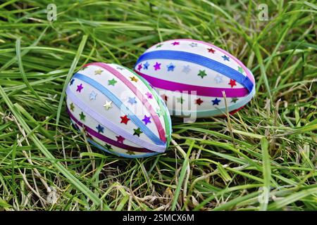 Two easter eggs, decorated with multicolored braid and sparkles as asterisks on the green grass Stock Photo