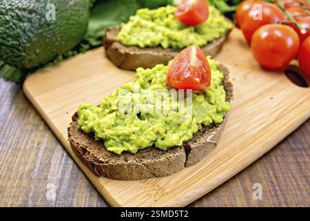 Two slices of rye bread with guakomole and tomato, avocado on the background dark wooden boards Stock Photo