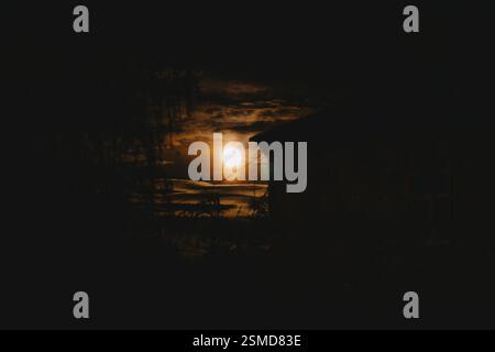 Full moon in a dark sky with silhouetted building and clouds Stock Photo