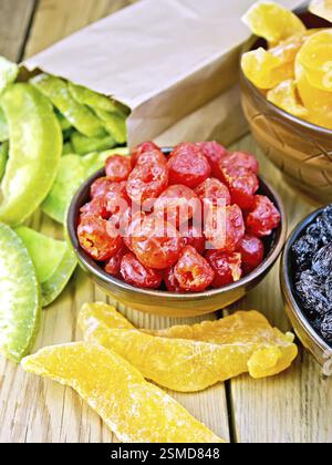 Candied cherries, melons, raisins in bowls, candied pomelo in a paper bag on a wooden boards background Stock Photo