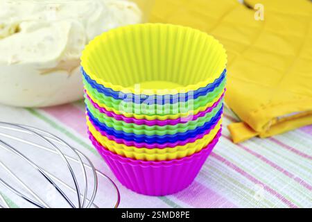 Colorful silicone molds for cupcakes, mixer, yellow cloth potholder, the dough in a glass bowl on linen background Stock Photo