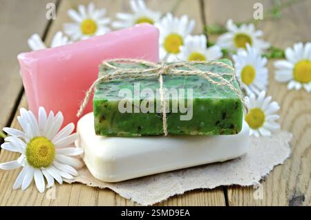 Three bars of soap pink, green and white on a piece of paper, daisy flowers on a background of wooden boards Stock Photo