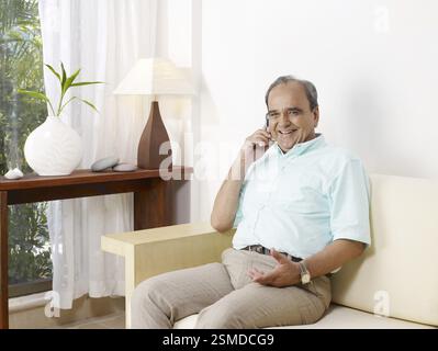 Old man talking on mobile sitting on sofa MR#702T Stock Photo