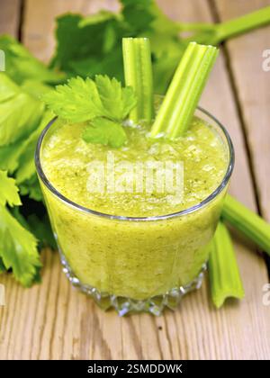 One glassful with a cocktail of celery and two petioles, stems and leaves of celery on a wooden boards background Stock Photo