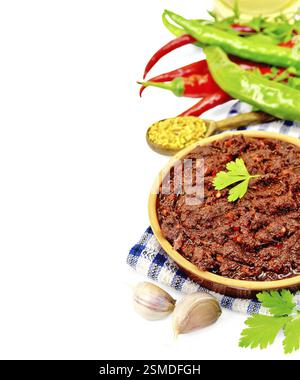 Tabasco adjika in clay cup on a napkin, hot pepper, garlic, parsley, fenugreek, oil in a carafe isolated on white background Stock Photo