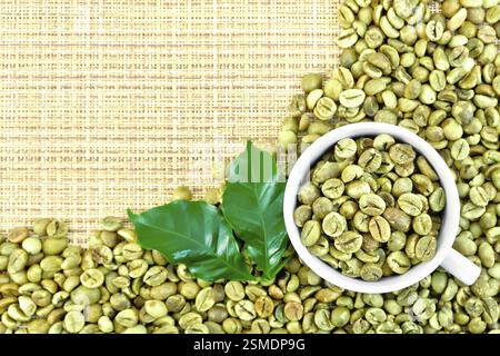 A frame of green coffee beans with leaves and a cup on a yellow coarse woven fabric Stock Photo