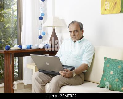 Old man in tension operating laptop sitting on sofa MR#702T Stock Photo