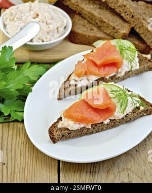 Sandwiches on two pieces of rye bread with cream, dill, cucumber and salmon in the oval plate on the background of wooden boards Stock Photo