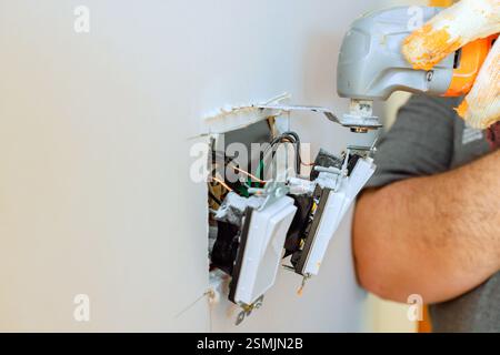 An electrician is repairing wall socket, using multi tools for electrical wires in residential environment. Stock Photo
