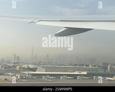 Airplane wing soars over a dazzling tapestry of Dubai's night lights, a glimpse into a new adventure from a cozy airplane window. Stock Photo