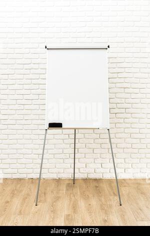 Flip chart set up against a white brick wall in a well-lit indoor space for a business meeting or presentation Stock Photo
