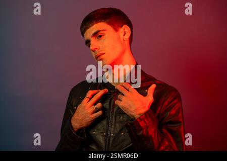 Fashionable young man wearing black leather jacket posing in studio with red and blue lighting Stock Photo