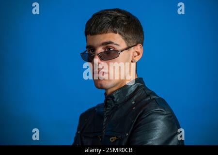 Fashionable young man with sunglasses and leather jacket posing on vibrant blue background Stock Photo