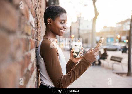 Happy young woman enjoys a coffee break while checking her phone in a city street Stock Photo