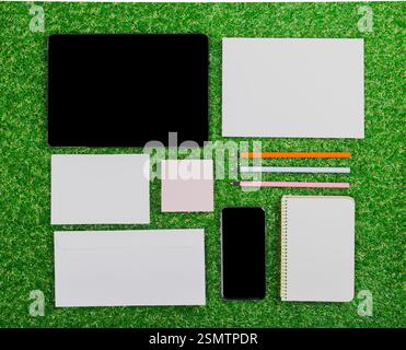 Organized workspace featuring digital devices, stationery, and notebooks on vibrant green grass Stock Photo