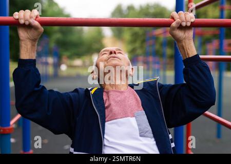 Sportive old man doing pull-ups outdoors Stock Photo