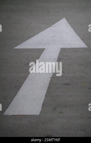 White arrow pointing ahead on concrete car park floor Stock Photo