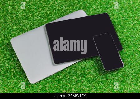 Multiple electronic devices arranged on green grass in a modern outdoor setting during daylight hours Stock Photo