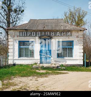 Old food store building in a village. White one-storey grocery shop with blue doors and window frames. Shop closed for a weekend. Stock Photo