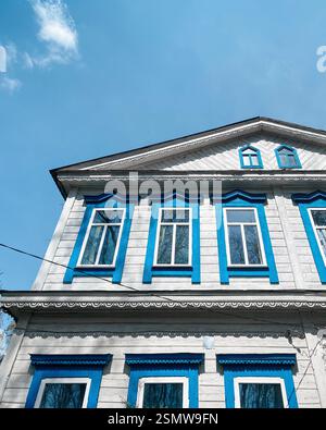 Old two-story house with white painted facade and blue window surrounds against clear blue sky. Stock Photo