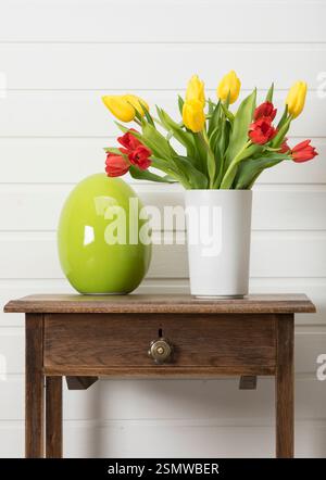 Bouquet of red and yellow tulips in a vase and green easter egg on a side table Stock Photo