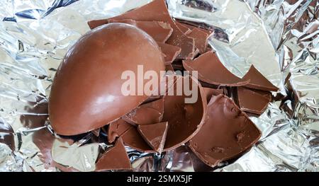 One milk chocolate Easter egg cracked in pieces on foil silver background. Easter and holiday season. Stock Photo
