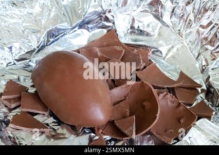 One milk chocolate Easter egg cracked in pieces on foil silver background. Easter and holiday season. Stock Photo