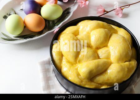Easter sweet bread, cozonac or tsoureki on table and colorful Easter eggs on a white wooden. Braided brioche, festive traditional dessert. Stock Photo