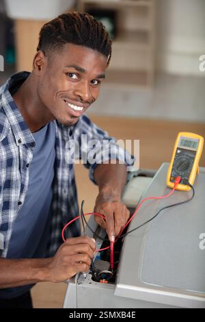 male service-agent testing washing machine with a multimeter Stock Photo