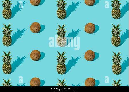 Trendy sunlight summer fruit pattern made of coconuts and pineapples on light blue background. Nature summer concept. Summer fruit aesthetic. Stock Photo