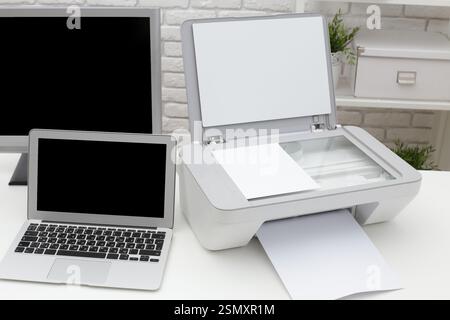 Printer and laptop setup on a modern desk in a cozy workspace during daylight hours Stock Photo