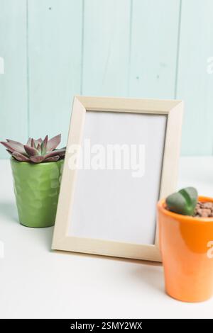 Minimalistic tabletop display featuring empty frame and potted succulents in vibrant planters against a soft background Stock Photo