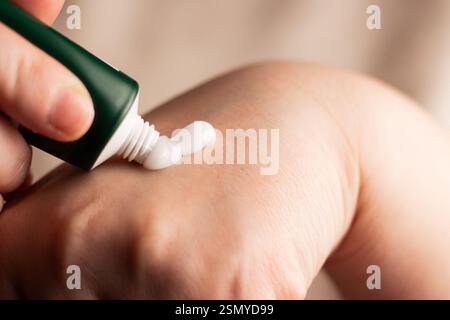 Woman applying hand cream on hands. Close up image of white cream. Squeeze cream out of tube. Soft hands and skincare concept. Stock Photo