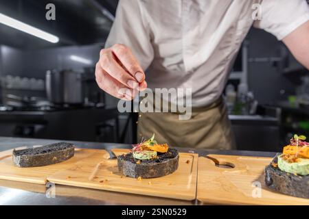 Chef sprinkling spices on gourmet black bread canapes in restaurant kitchen Stock Photo