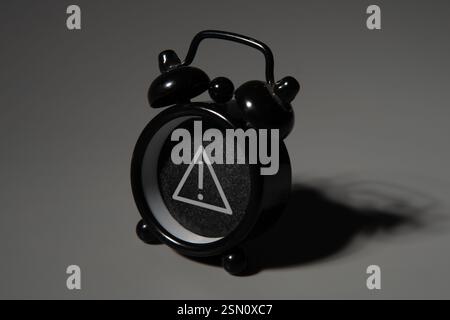 A black alarm clock with a white exclamation mark on a dark background. Warning, alert, caution concept. Stock Photo