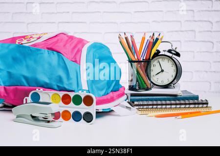 Colorful school supplies arranged neatly on a table with a backpack, stationery, and an alarm clock during a study session Stock Photo