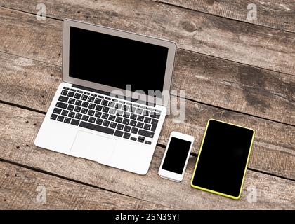 Various electronic devices arranged on a rustic wooden table during daylight Stock Photo
