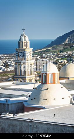A Santorini bell tower rises against the endless blue sky, its white arches glowing in the sunlight. The deep blue accents blend with the Aegean Sea Stock Photo