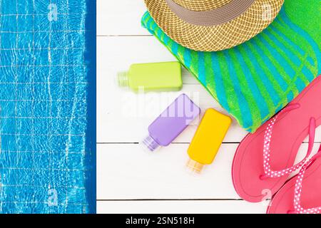 Relaxing at a pool with colorful towels, flip flops, and sun care items on a sunny day Stock Photo