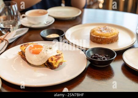 A fried sunny-side-up egg topped with black pepper sits beautifully on melted cheese toast, served on a white plate. Perfect for promoting breakfast m Stock Photo