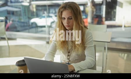 Woman working on laptop in modern office with sunlight filtering through large windows, showcasing a focused professional environment with relaxed atm Stock Photo