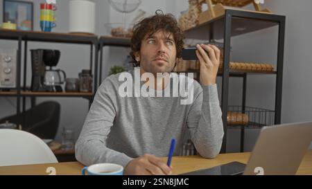 Young man listens to voice message in a modern office while taking notes displaying a focused expression in a stylish indoor setting surrounded by con Stock Photo