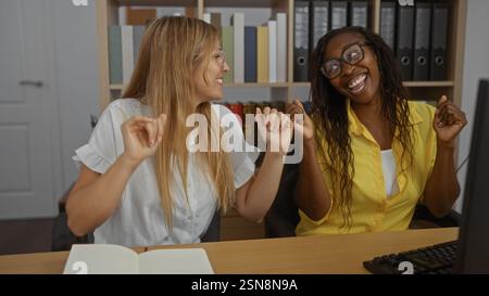 Two women dancing joyfully in an office, capturing a lively moment between coworkers in a professional indoor setting. Stock Photo
