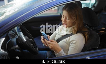 Woman driving in urban environment using smartphone in car wearing sweater and seatbelt, demonstrating modern lifestyle and technology interaction. Stock Photo