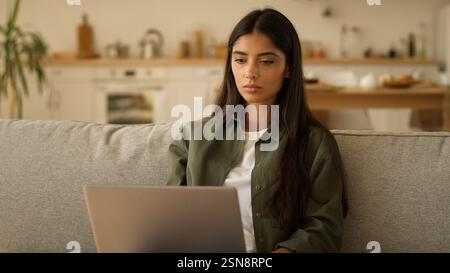 Concentrated Arabian woman Indian freelancer girl student female Hispanic lady at home couch working laptop distant studying computer remote work pc Stock Photo