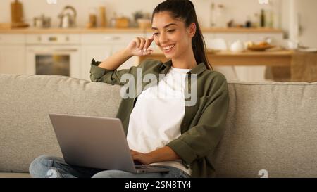 User freelance worker at home couch student receive good exams result online woman Indian girl Arabian female win laptop using browsing computer Stock Photo