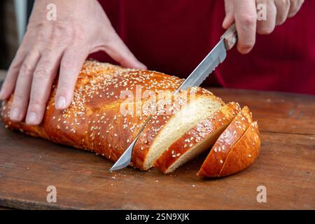 Easter sweet bread, cutting a tsoureki braid in slices on wooden table, closeup view Stock Photo
