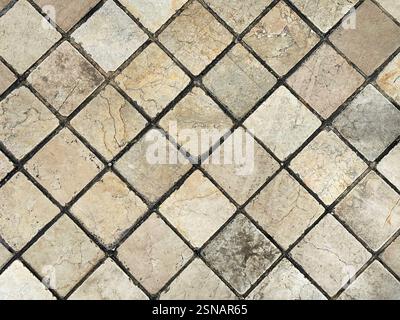 Natural stone marble tiles in diamond shape pattern. Outdoor honed tiles with random veins in yellow and beige color with black grouts.  wall or floor Stock Photo