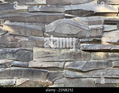 Striped cut combed andesite stone wall cladding stacked on one another. Andesite stone or lavastone for outdoor architectural wall finishing, in grey Stock Photo