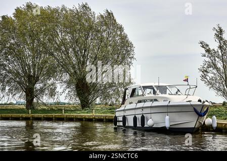 A cabin cruiser motorboat named Spyglass moored alongside a grassy riverbank on the Norfolk Broads, England. Stock Photo